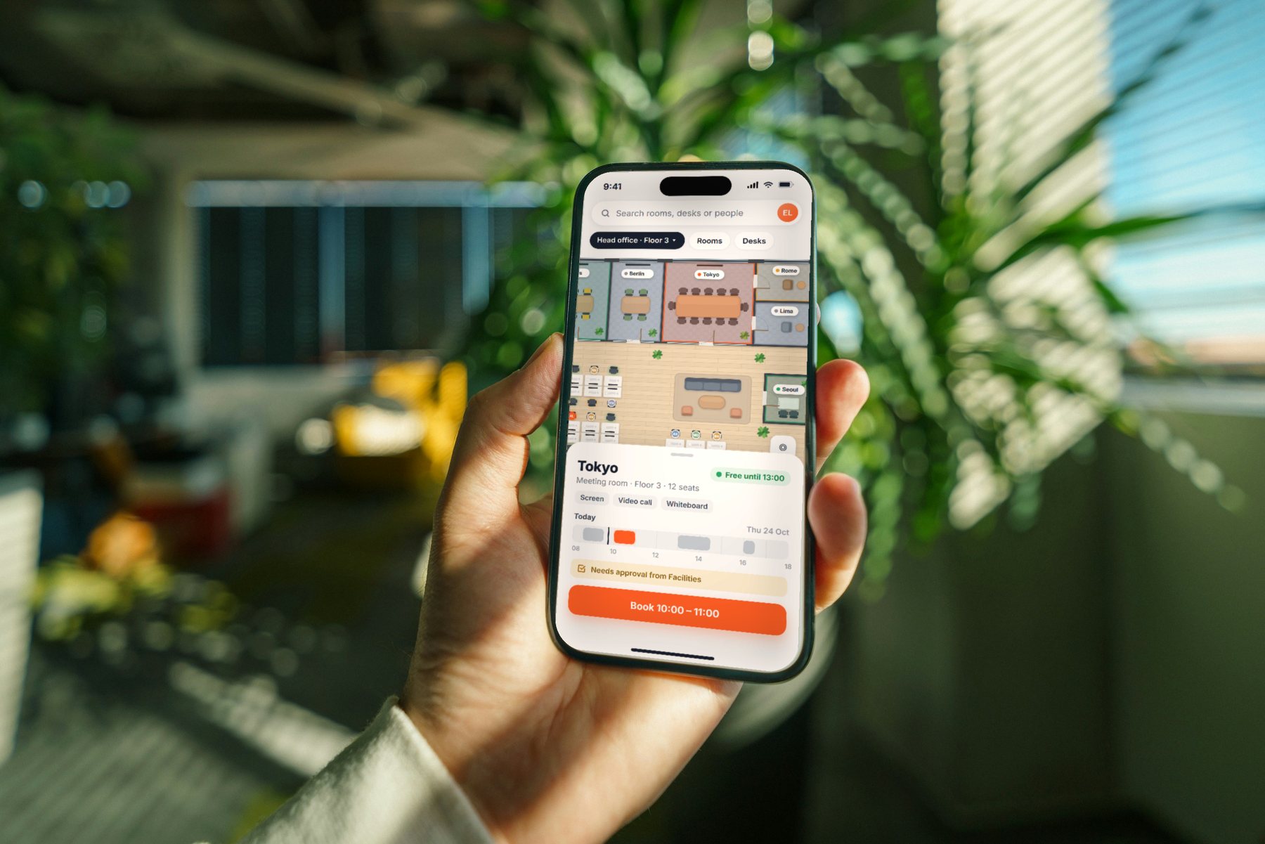 En hand håller en mobil med YesDesk-appen: planritningen, mötesrummet Malmö markerat och dagens schema.